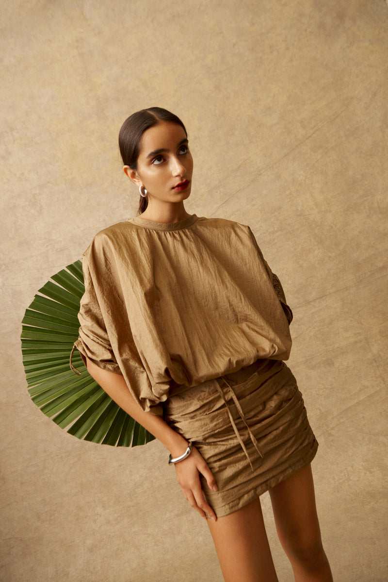 Woman wearing a beige outfit against a beige background with a green leaf decoration.